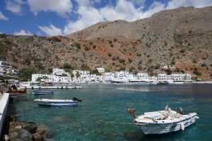 Kleine Boote im Hafen von Loutro auf Kreta mit weißen Häusern in Hintergrund.