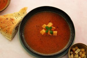 Geröstete Gemüsesuppe mit Croutons und Brot serviert.