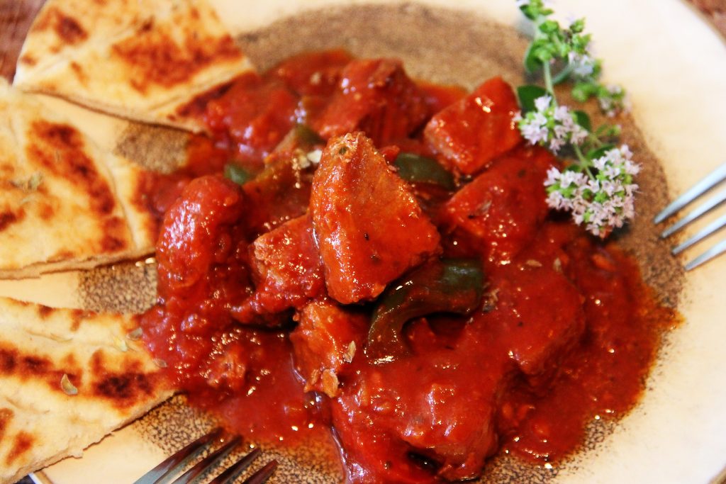Bekri Meze angerichtet auf einem hellen Teller mit Pita. Oregano mit Blüten als Deko.