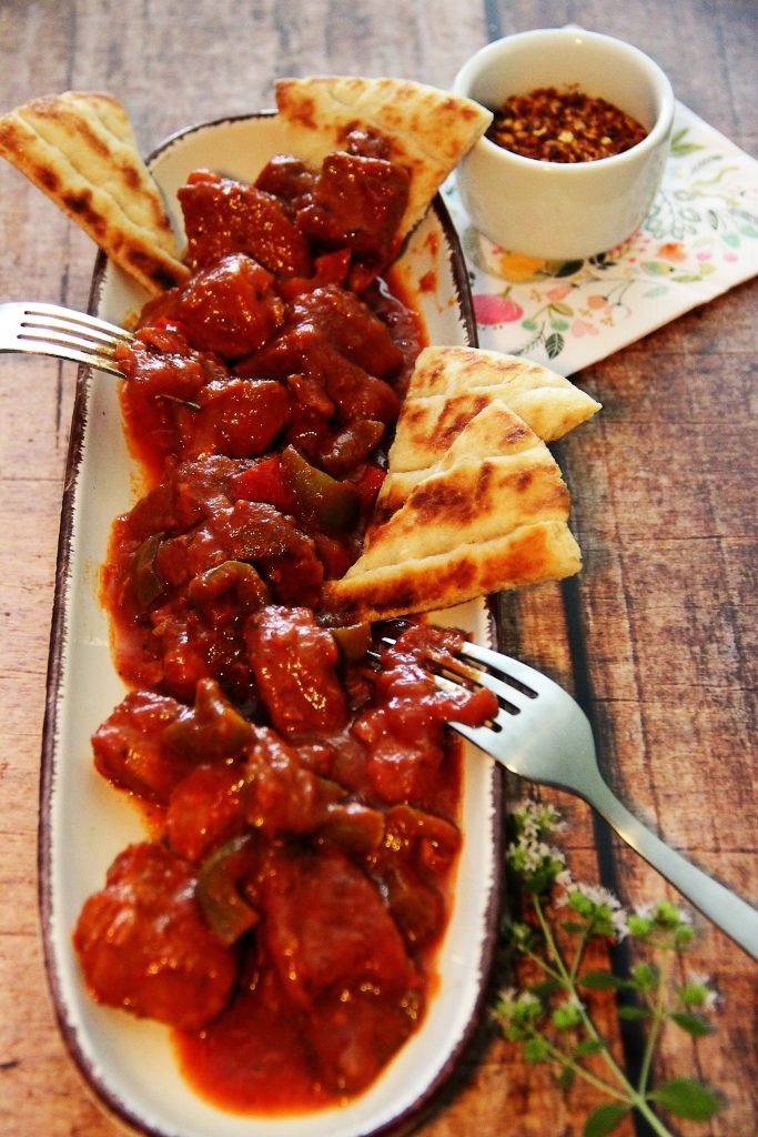 Bekri Meze angerichtet auf einem schmalen, hellen Teller mit Pita. Chili und Oregano als Deko.