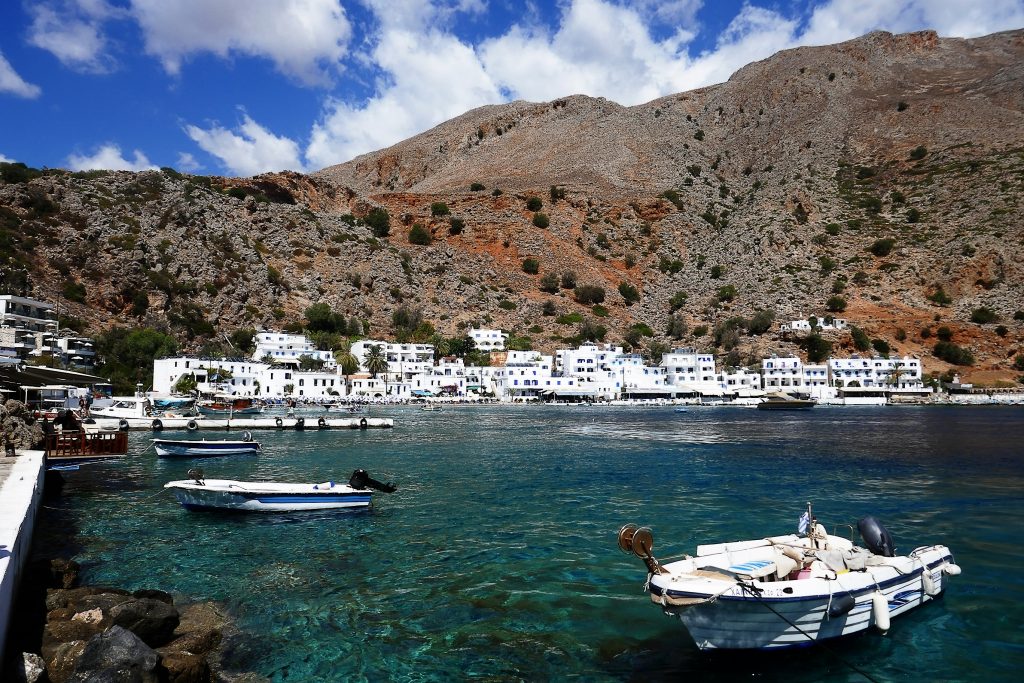 Kleine Boote im Hafen von Loutro auf Kreta mit weißen Häusern in Hintergrund.
