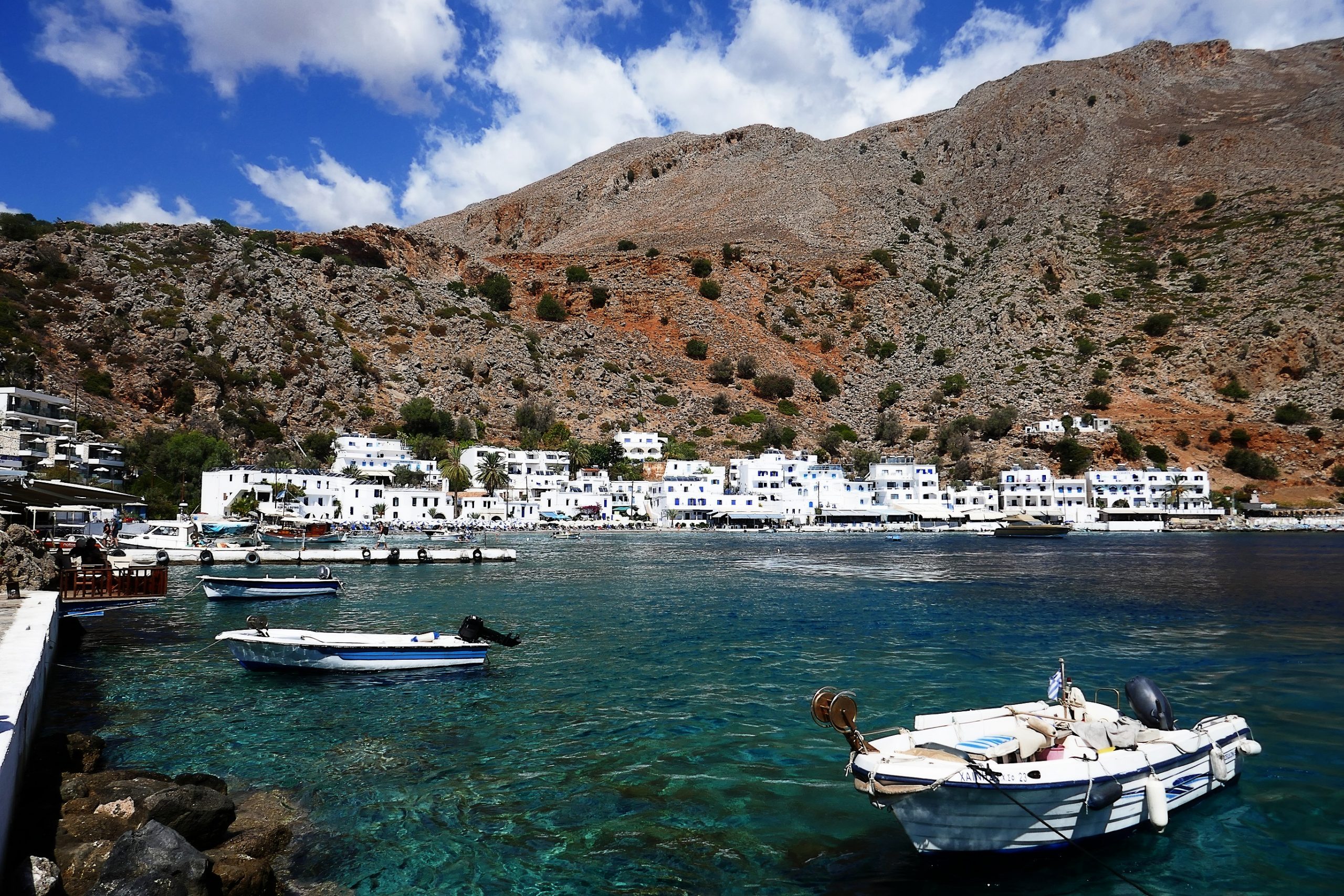 Kleine Boote im Hafen von Loutro auf Kreta mit weißen Häusern in Hintergrund.